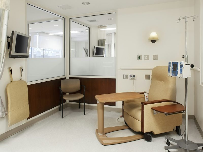 Interior view of a hospital treatment cubicle with a chair and a drip treatment stand.